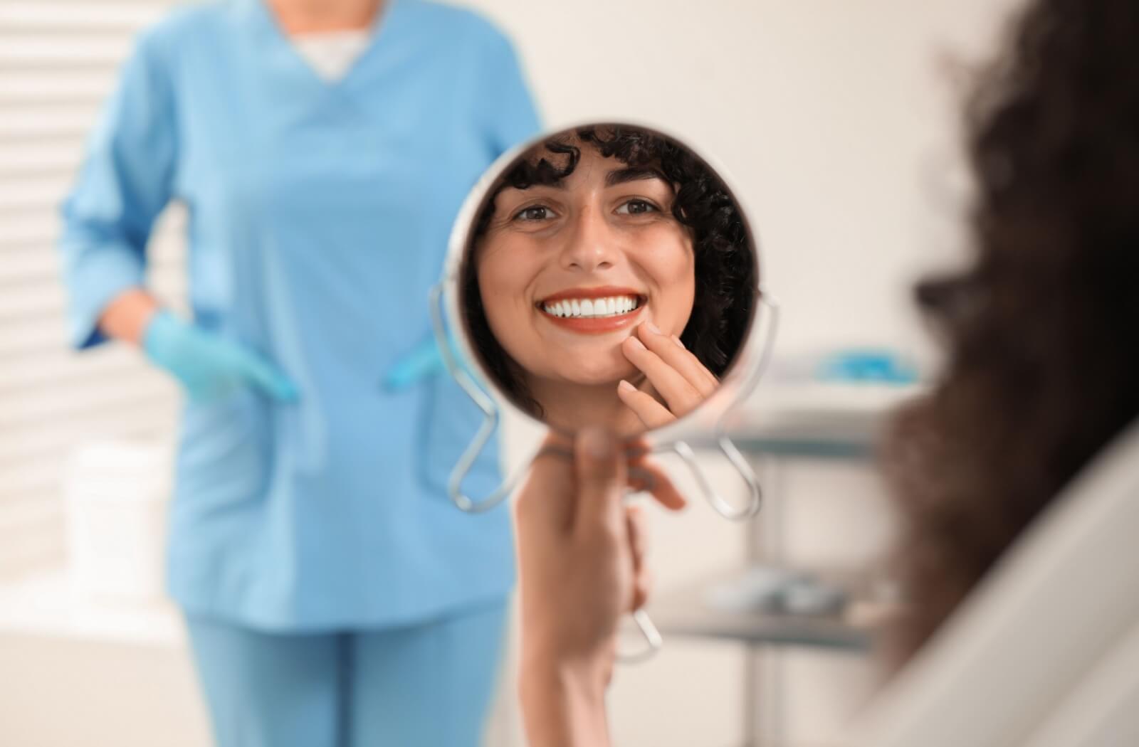 A patient looking into a handheld mirror to admire her bright, straight smile after a dental procedure.